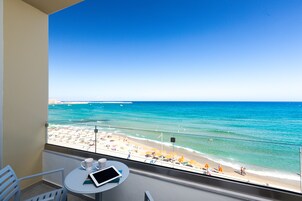 Un balcón con vista a la playa, una mesa con una tablet y una taza, y una silla.