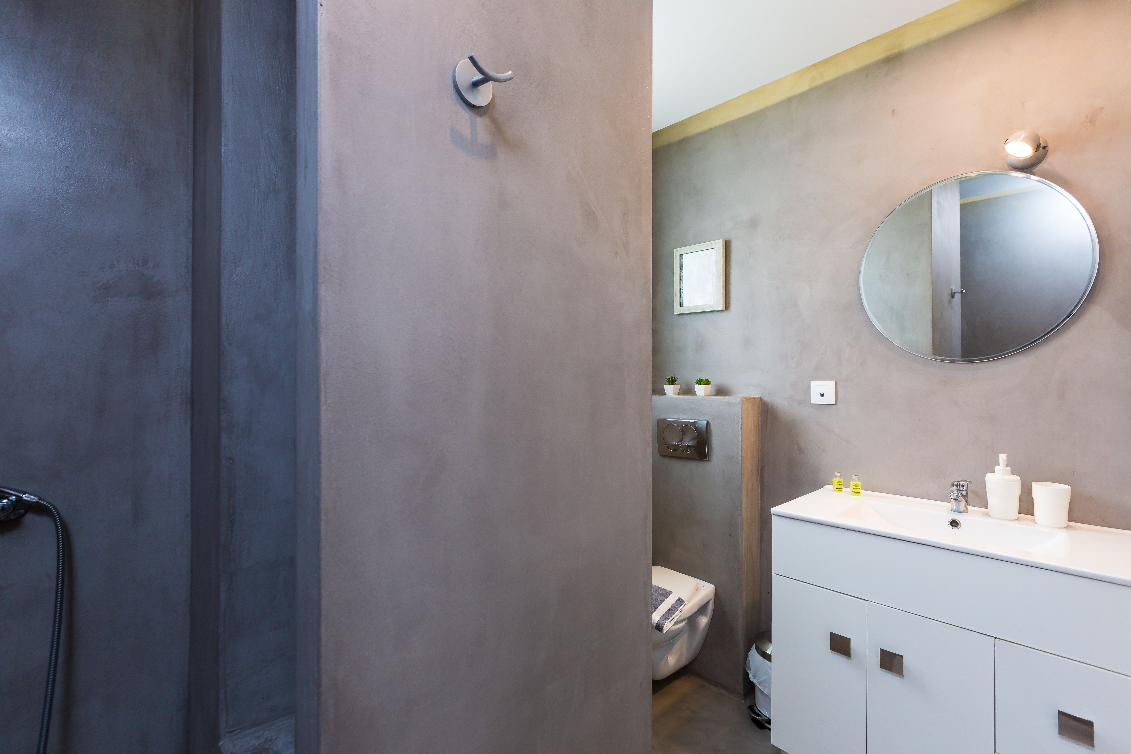 A bathroom with a modern design, featuring a white vanity, a round mirror, and a toilet.