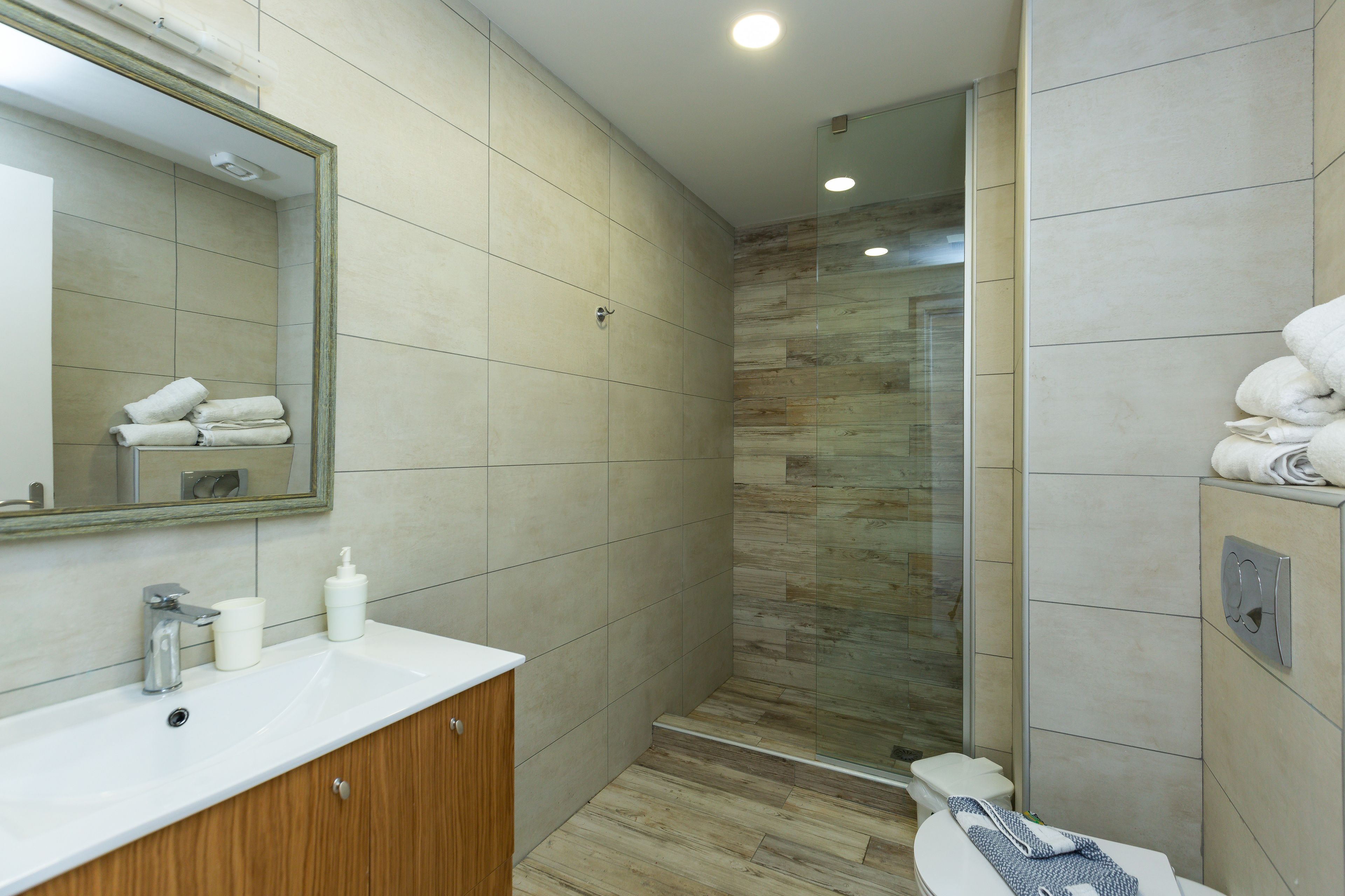 A modern bathroom with a white sink, wooden cabinet, and a glass shower enclosure.