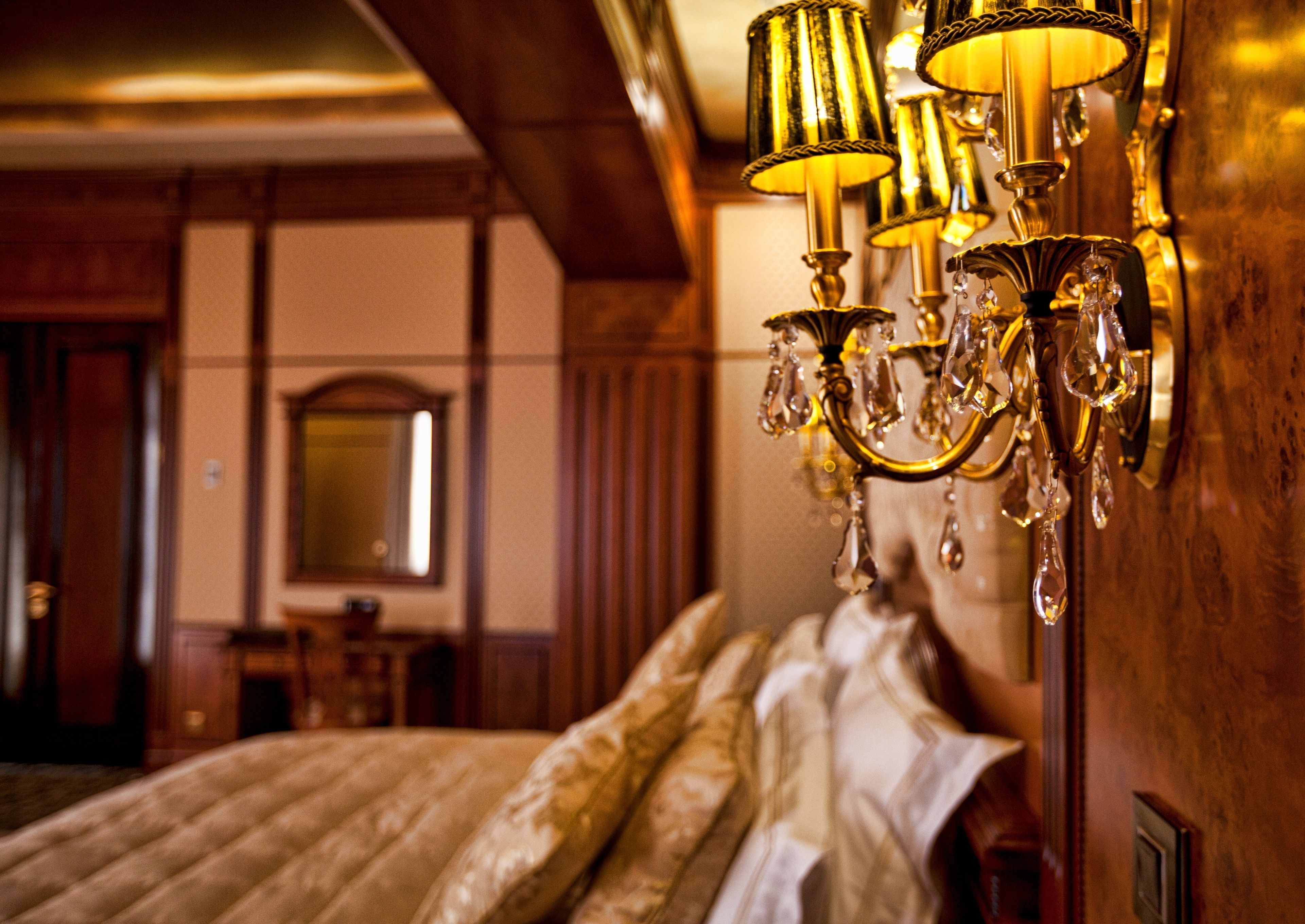 A hotel room with a large bed, a chandelier, and wooden paneling.