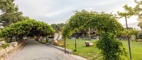 A cobblestone pathway leading to a gazebo with a canopy, surrounded by lush greenery and outdoor seating.