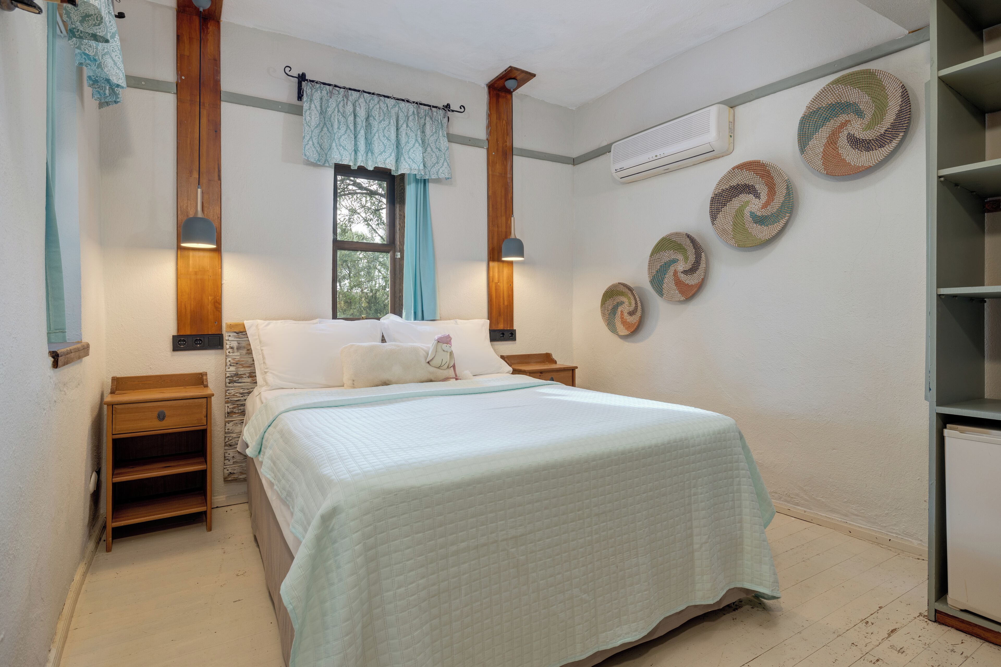A bedroom with a bed, nightstands, a window with curtains, wall art, and an air conditioning unit.