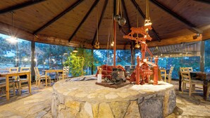 A rustic interior with a stone central feature, wooden furniture, and large windows offering views of the outdoors. - Aral Tatil Ciftligi (Bozcaada)