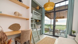 A room with a wooden desk, a chair, a sofa, a large window with a view, and a hanging light fixture. - Aral Tatil Ciftligi (Bozcaada)