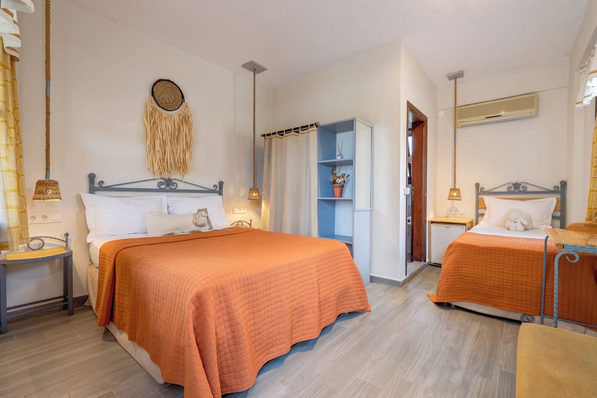 A bedroom with two beds, a bedside table with a lamp, a wardrobe, and a wall-mounted air conditioner.