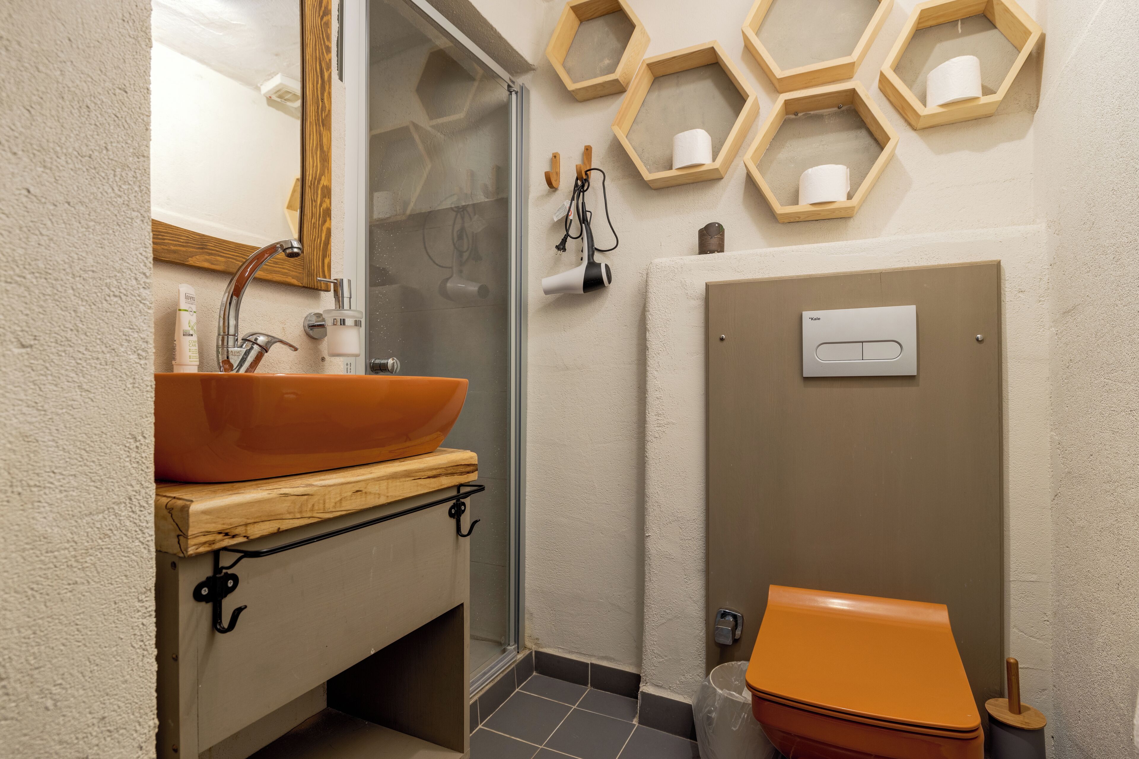 A bathroom with a large vessel sink, a glass shower enclosure, and a toilet with a wooden vanity.