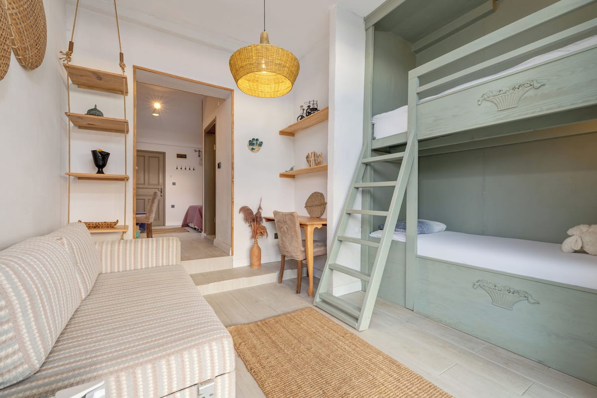 A cozy room with a bunk bed, a sofa, a dining table, and a hanging light fixture.