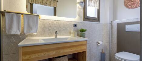A bathroom with a wooden vanity, a white sink, a mirror, a toilet, and a towel rack.