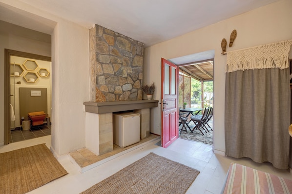 A room with a stone fireplace, a red door, and a view of an outdoor patio. - Aral Tatil Ciftligi (Bozcaada)