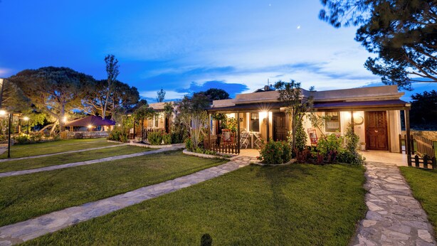A residential property with a stone pathway, well-maintained lawn, and a covered outdoor seating area. - Aral Tatil Ciftligi (Bozcaada)