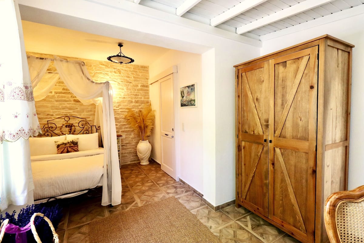 A bedroom with a bed, a wooden wardrobe, a stone wall, and a ceiling fan.