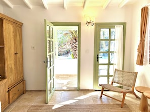 A room with a wooden cabinet, a wicker chair, and two doors leading to an outdoor area. - Kemerbag 29 - Adults Only (Bozcaada)