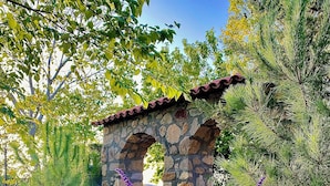 Un arco de piedra con techo de tejas, rodeado de follaje y plantas con flores.