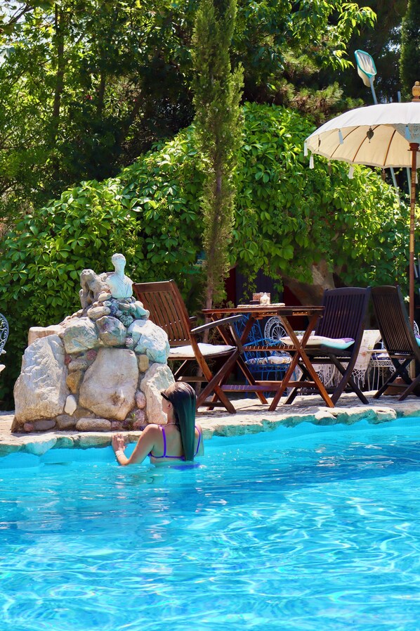 Una piscina con sillas de descanso y una mesa, rodeada de abundante vegetación.