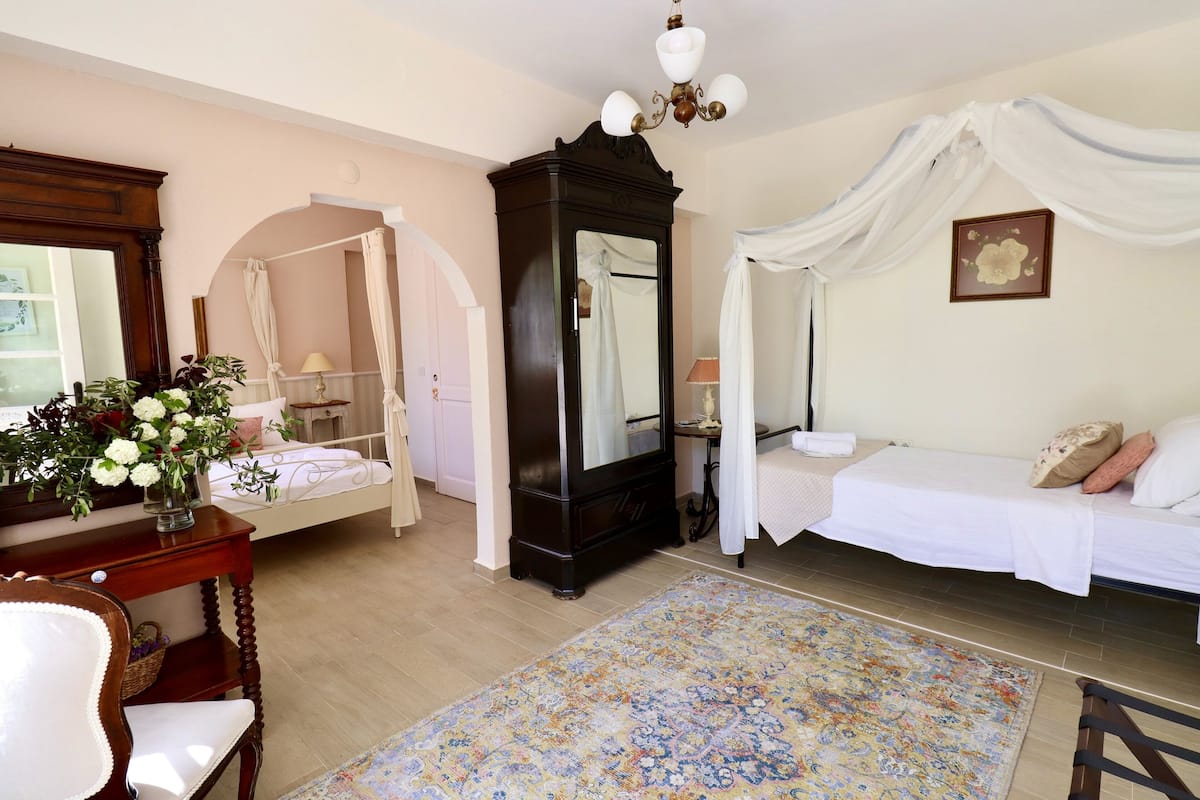 A bedroom with a canopy bed, a large mirror, a wooden dresser, and a floral rug.