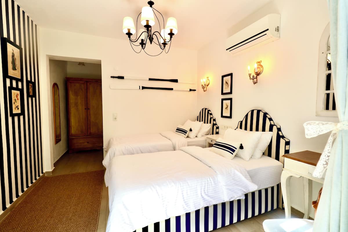A bedroom with two beds, a desk, a chandelier, and wall-mounted lights.