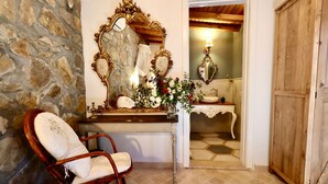 Una habitación con pared de piedra, una silla de madera, un tocador con espejos ornamentados y un guardarropa de madera.