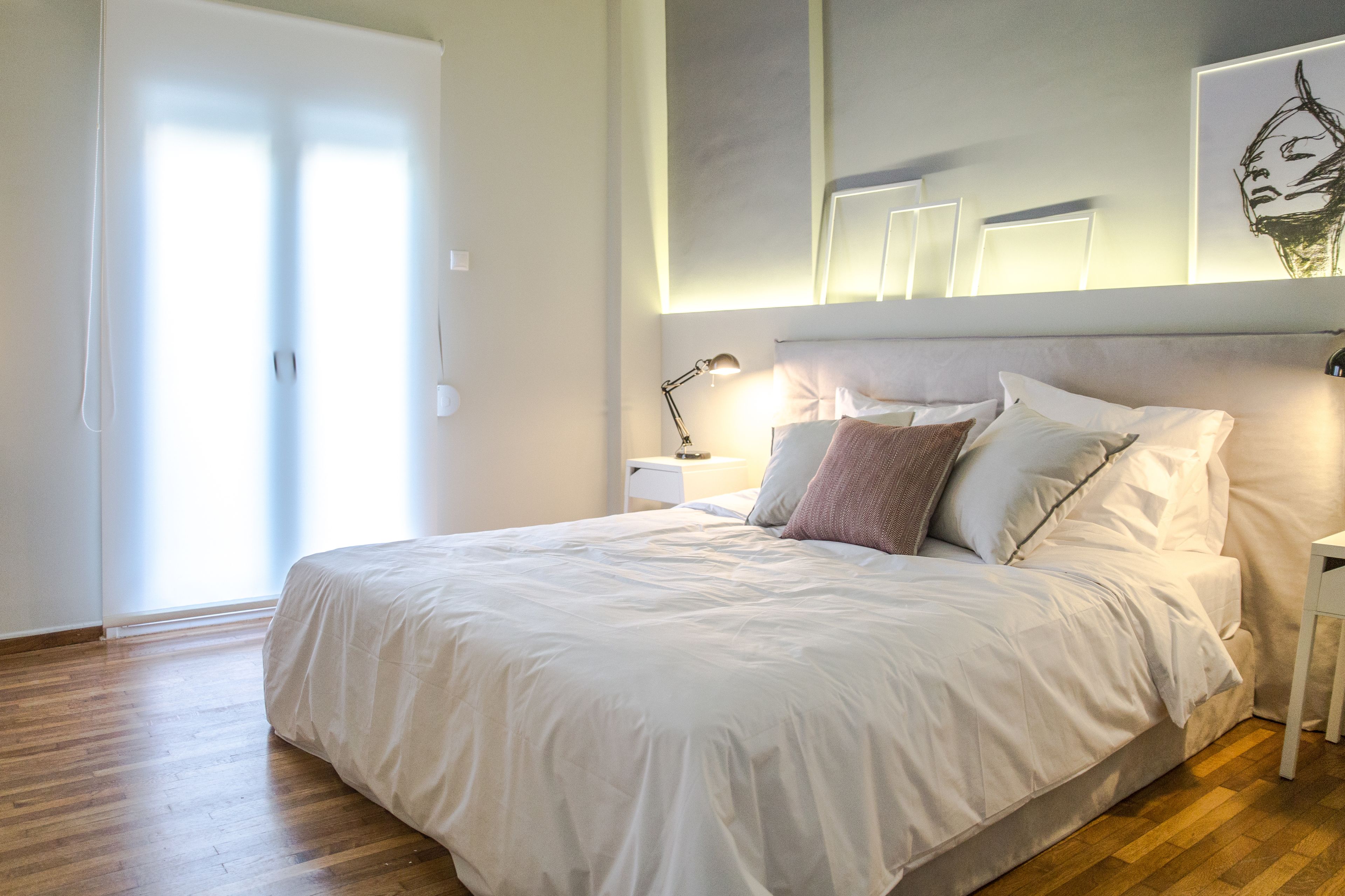 A neatly made bed with white bedding, a bedside lamp, and a wall-mounted artwork.