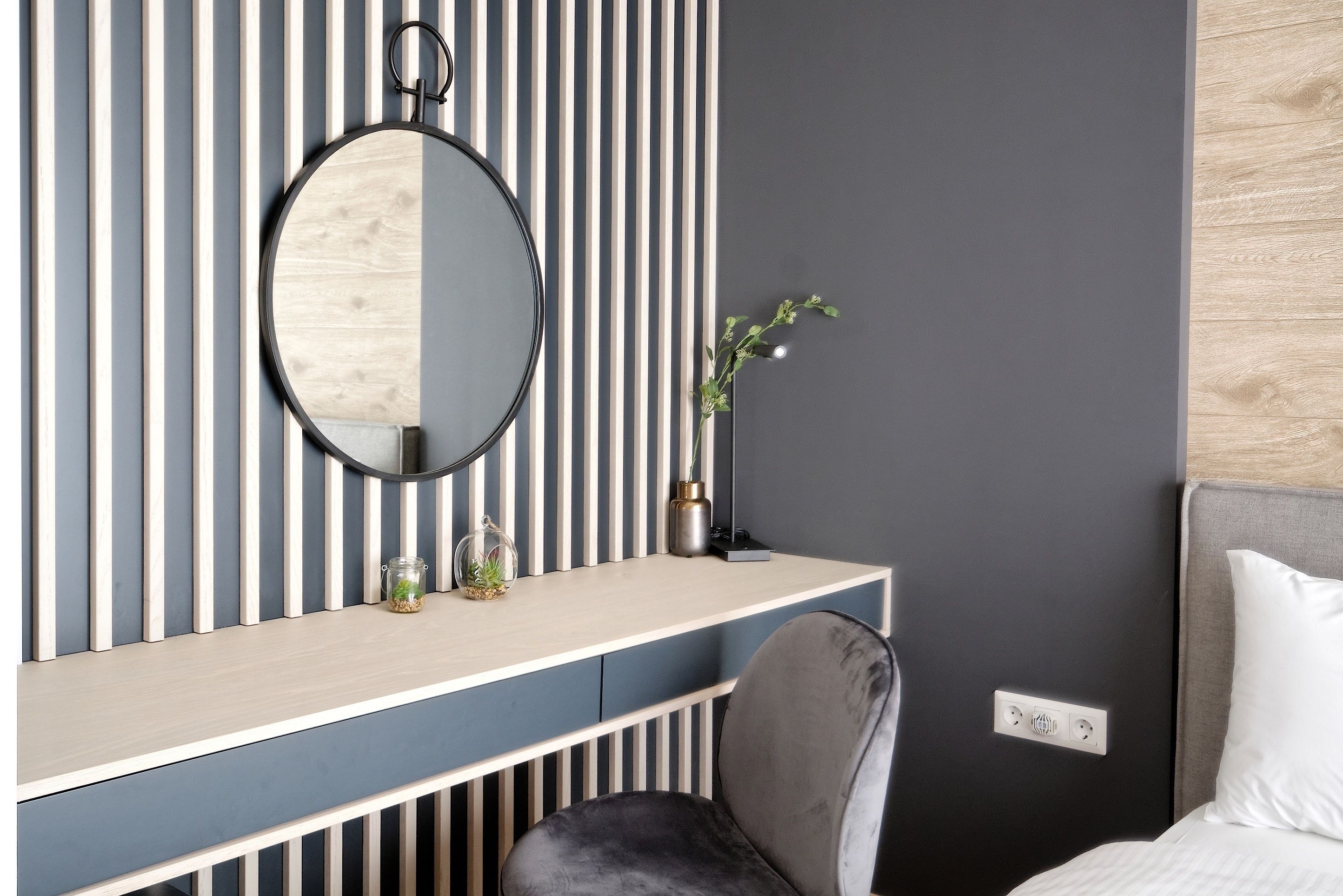 A modern room with a striped wall, a round mirror, a small plant, and a grey chair.