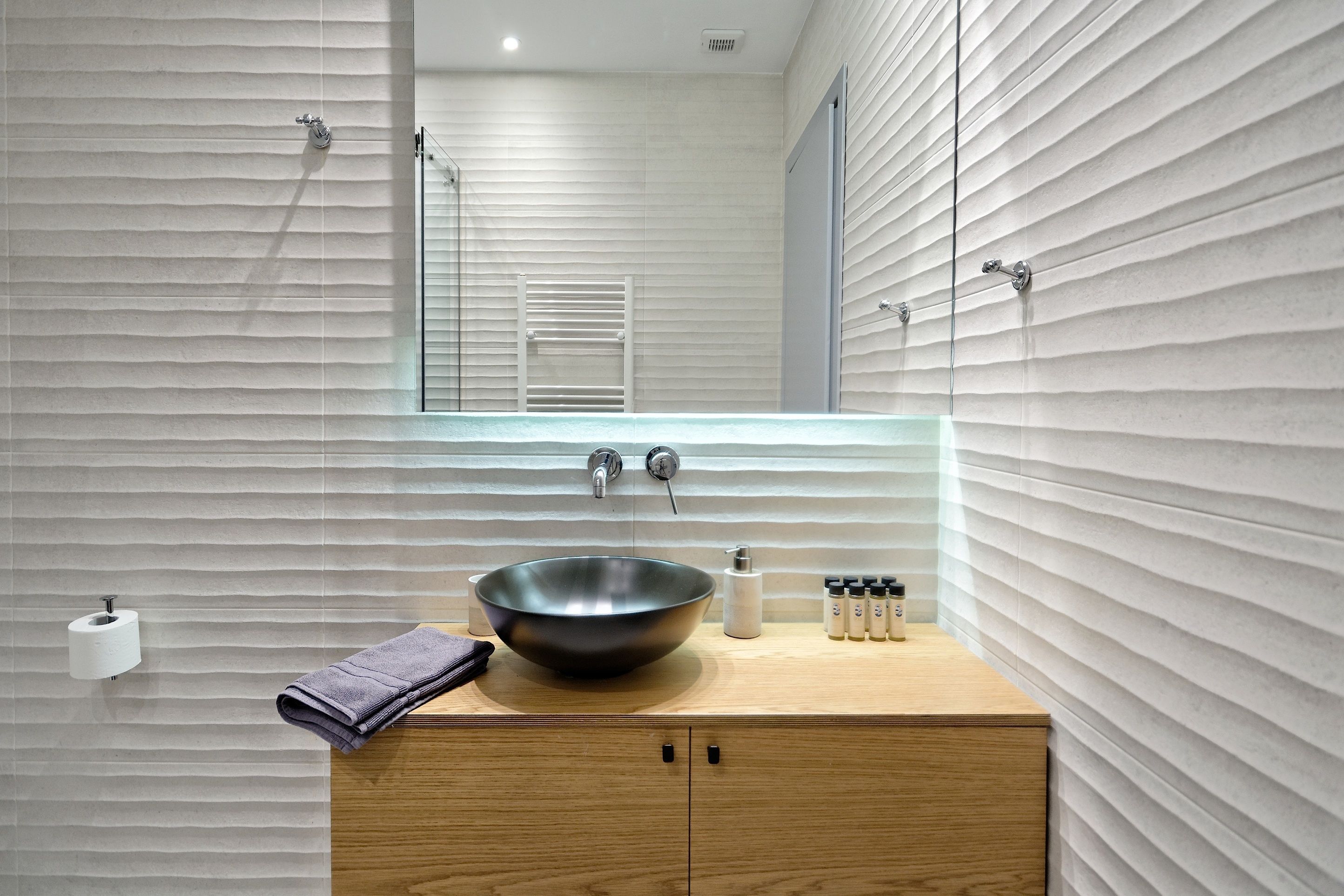 A modern bathroom with a wooden vanity, a large vessel sink, and a mirror above it.