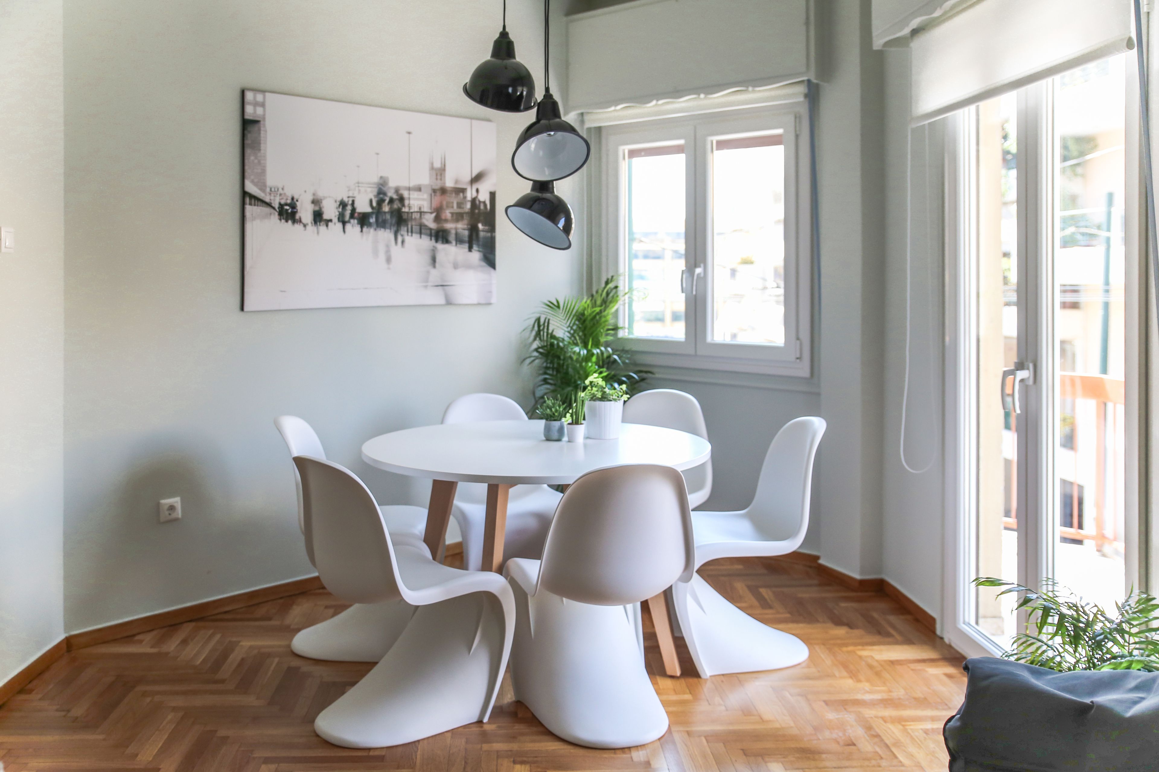 A dining area with a round table, white chairs, a potted plant, and a cityscape artwork on the wall.