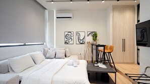Una habitación de hotel moderna con una cama, un pequeño comedor con mesa y sillas, una planta en maceta y un armario.