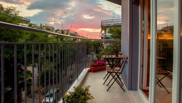 Un balcón con vistas al cielo, una mesa, sillas y plantas en macetas.
