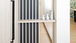 Un interior moderno con piso de madera, una puerta corrediza con persianas verticales y una pequeña mesa blanca con objetos decorativos.