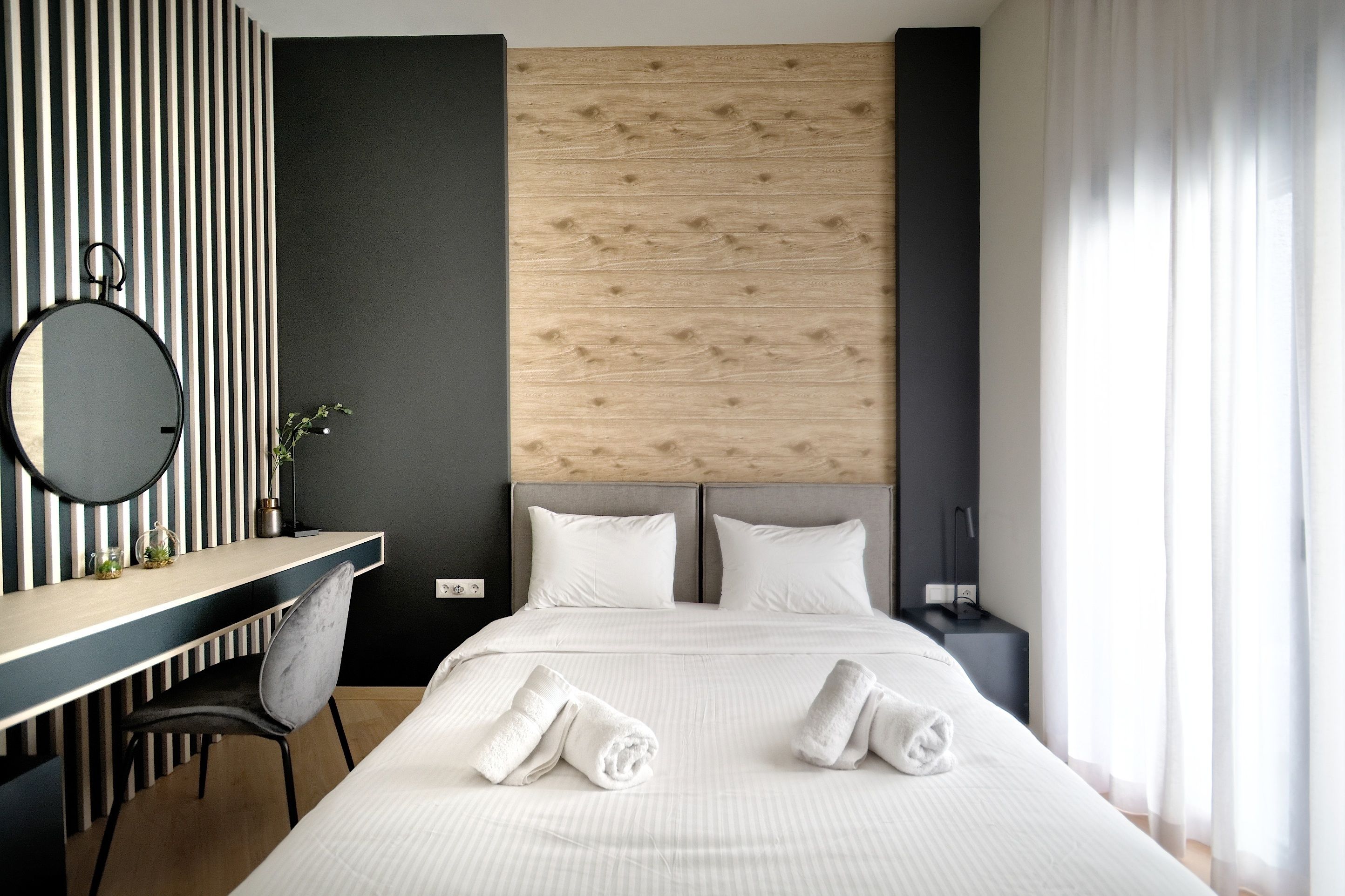 Een moderne hotelkamer met een houten hoofdbord, een bureau met stoel, en een bed met keurig opgevouwen handdoeken.
