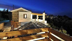A modern house with a stone facade, a wooden deck, and a covered outdoor area. - OLIVIA VILLAS (Ikaria)