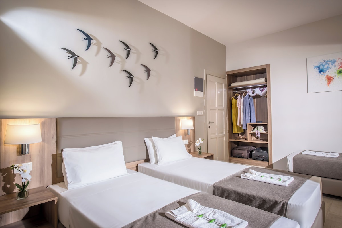 Ein Hotelzimmer mit zwei Betten, einem Schrank, einem Spiegel und einer Wand mit Vogeldekorationen.