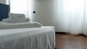 A neatly made bed with a white bedspread and a stack of folded white towels on top.