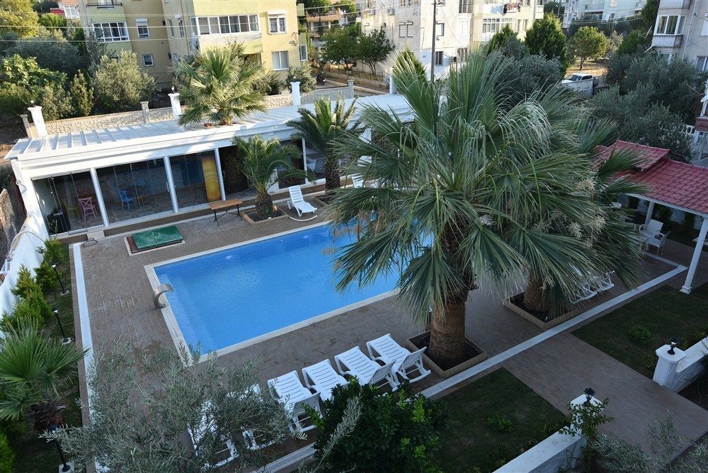 A rooftop swimming pool with lounge chairs, palm trees, and a view of surrounding buildings.