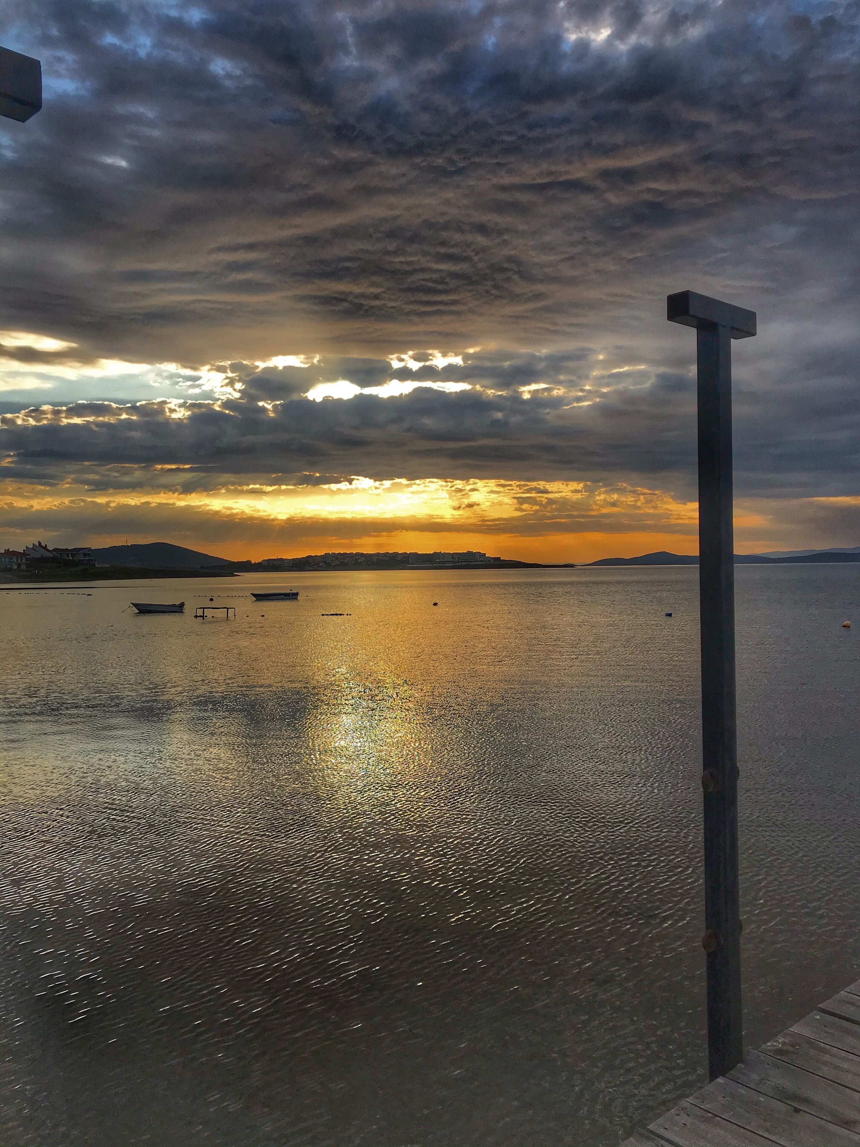 Une vue sur le front de mer, avec un quai et une structure en forme de croix, des eaux calmes et un coucher de soleil.