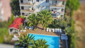 A two-story building with a swimming pool, sun loungers, and palm trees. - Uzunhan Hotel (Ayvalik)