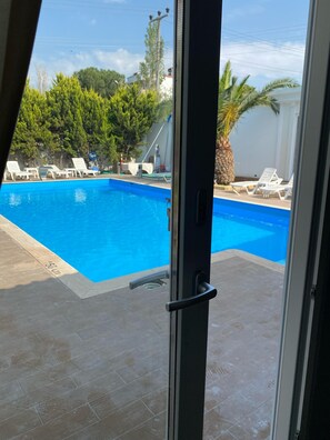 A view of a swimming pool with lounge chairs, a palm tree, and a clear sky. - Uzunhan Hotel (Ayvalik)
