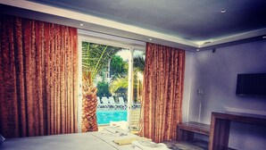 A hotel room with a large bed, a TV, and a view of a pool. - Uzunhan Hotel (Ayvalik)