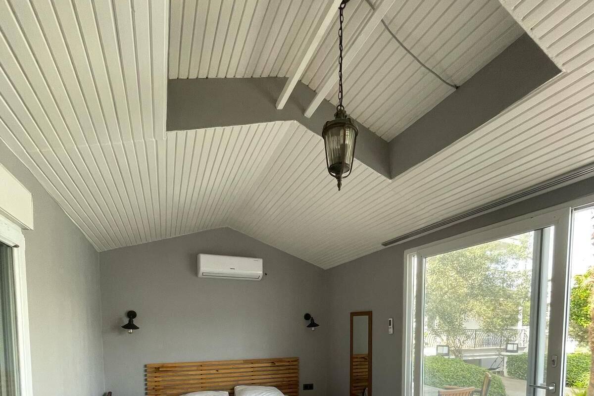 Une chambre à coucher avec un lit en bois, un ventilateur de plafond, une grande fenêtre et une vue sur l’extérieur.