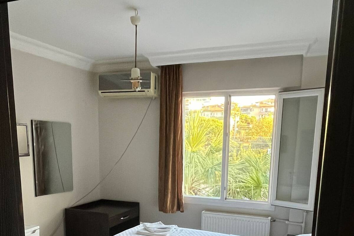 Une chambre d’hôtel comprenant un lit, un bureau, une chaise, une fenêtre avec des rideaux, un radiateur et un téléviseur fixé au mur.