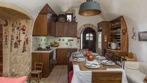 A cozy kitchen with wooden cabinets, a dining table set for four, and a hanging light fixture. - Villa Tzivaeri (Chania)