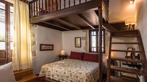 A bedroom with a wooden bed, a nightstand, a lamp, a window, and a wooden staircase. - Villa Tzivaeri (Chania)