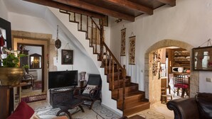 A cozy living room with a wooden staircase, a television, a comfortable chair, and a dining area with a table and chairs. - Villa Tzivaeri (Chania)