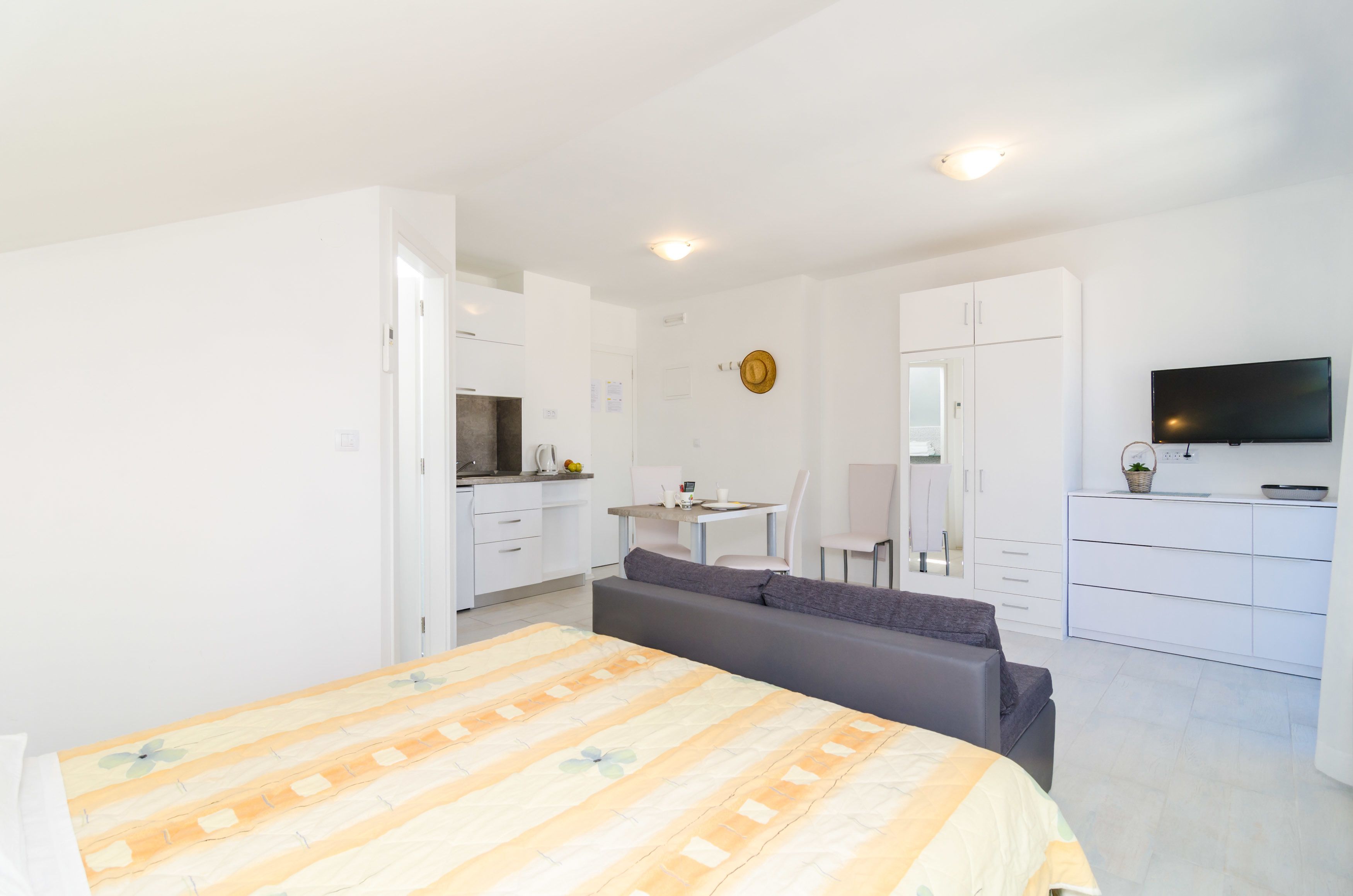 A modern bedroom with a bed, a sofa, a TV, and a kitchenette.