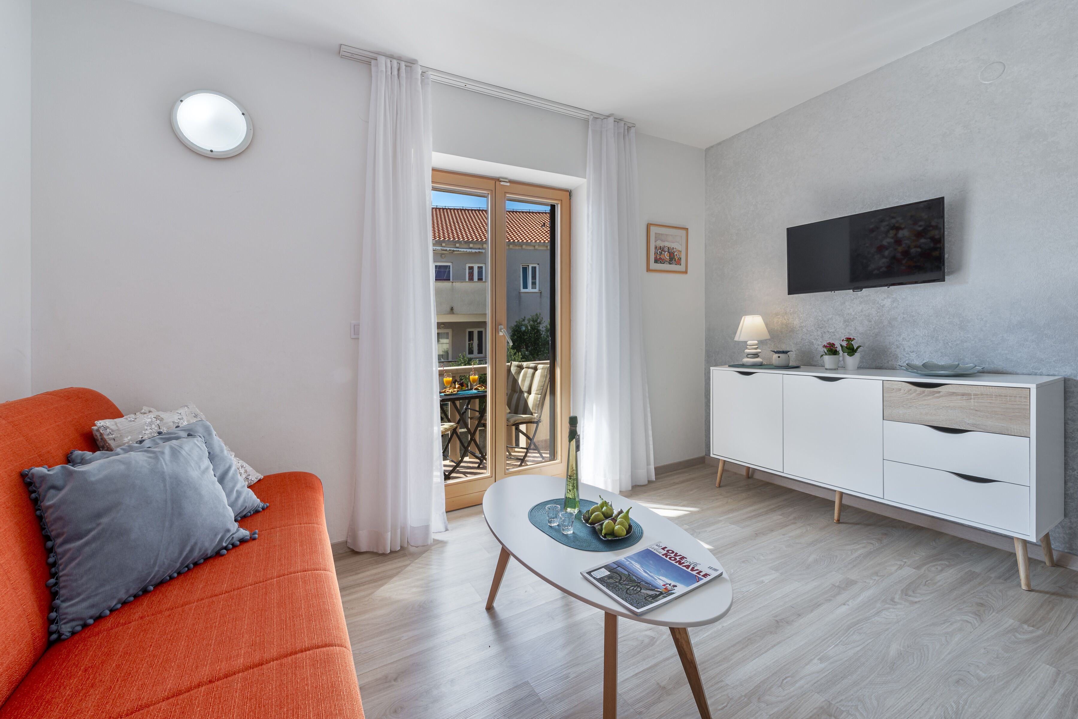Un soggiorno moderno con un divano, un tavolino da caffè con riviste, una televisione e una zona pranzo visibile tramite una porta in vetro.