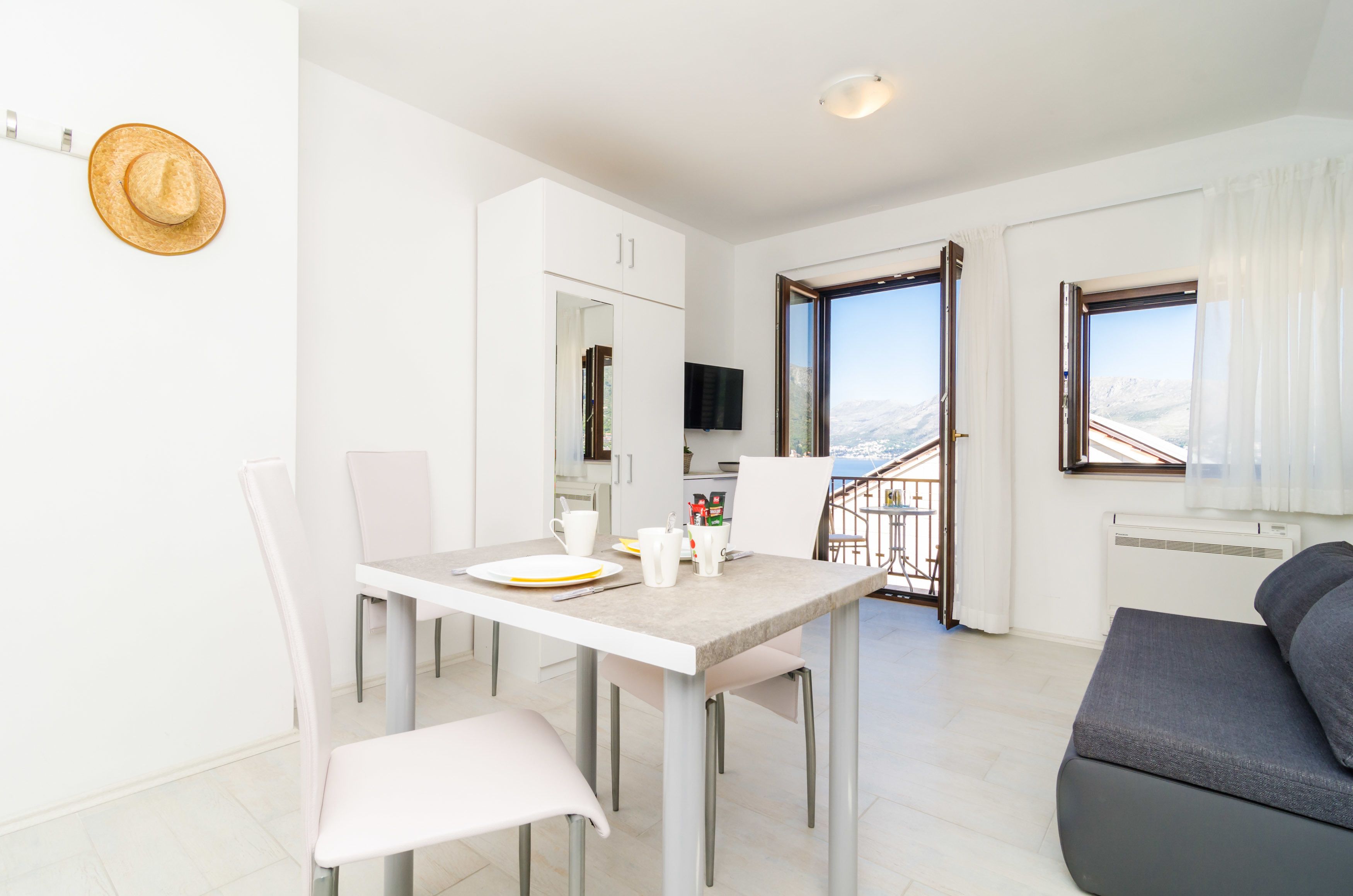 A modern kitchen with white cabinets, a dining table set for two, and a TV mounted above the counter.