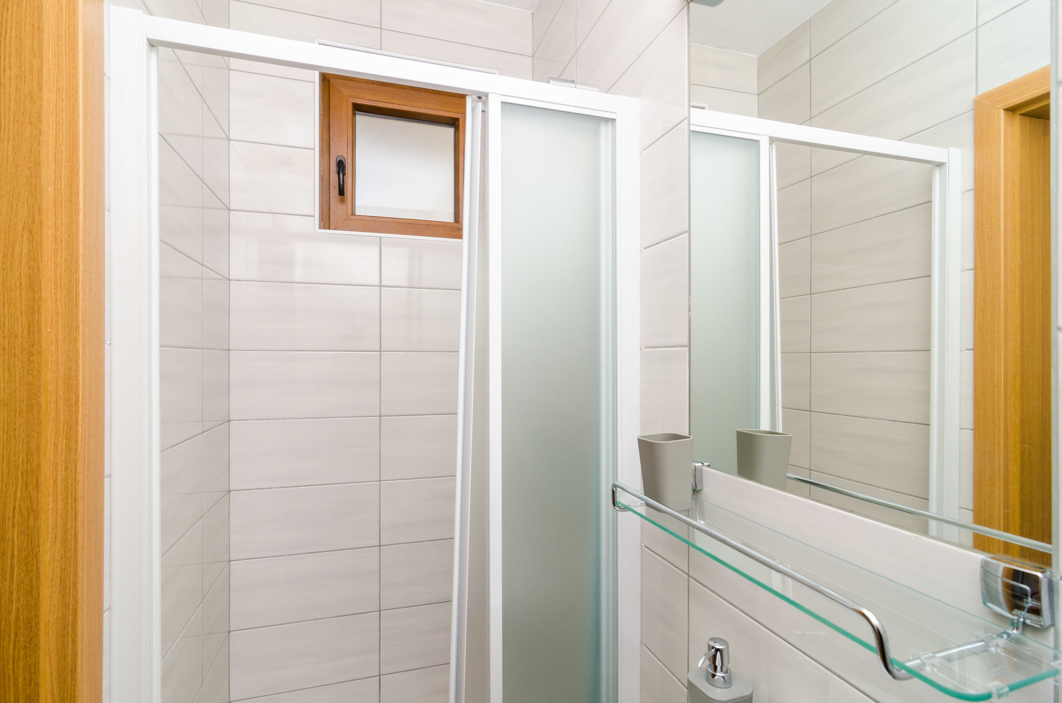 A modern bathroom with a glass shower enclosure, a wooden door, and a glass sink with a metal faucet.