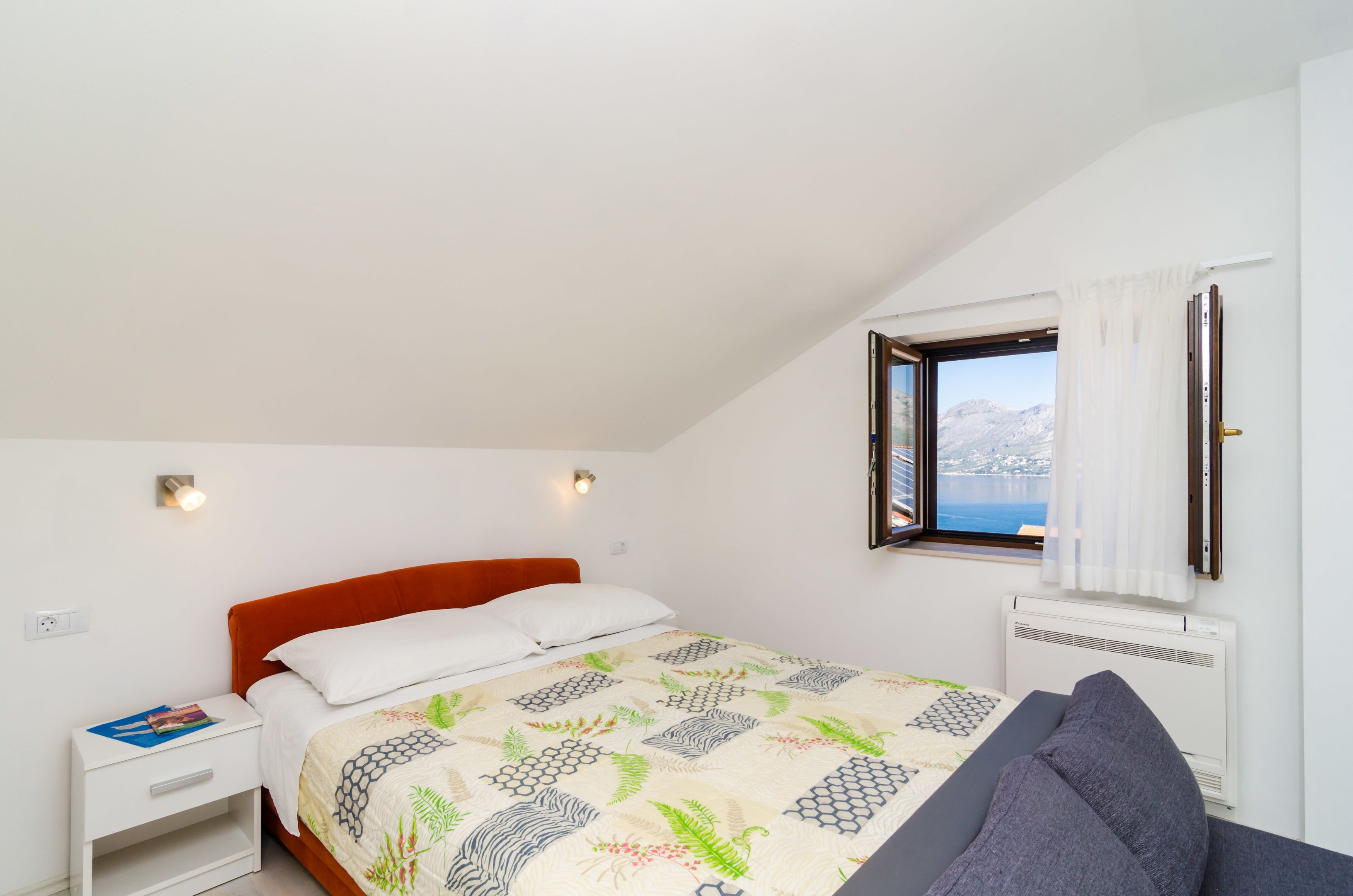 Quarto com cama, mesa de cabeceira, janela com vista e aquecedor fixado na parede.