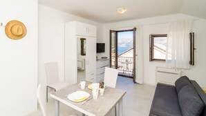 A modern living room with a sofa and a dining area with a table set for two. - Cina Apartments (Konavle)