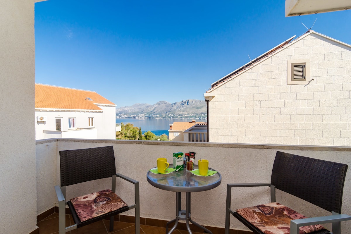 A balcony with two chairs and a table, overlooking a scenic view of a body of water and mountains.