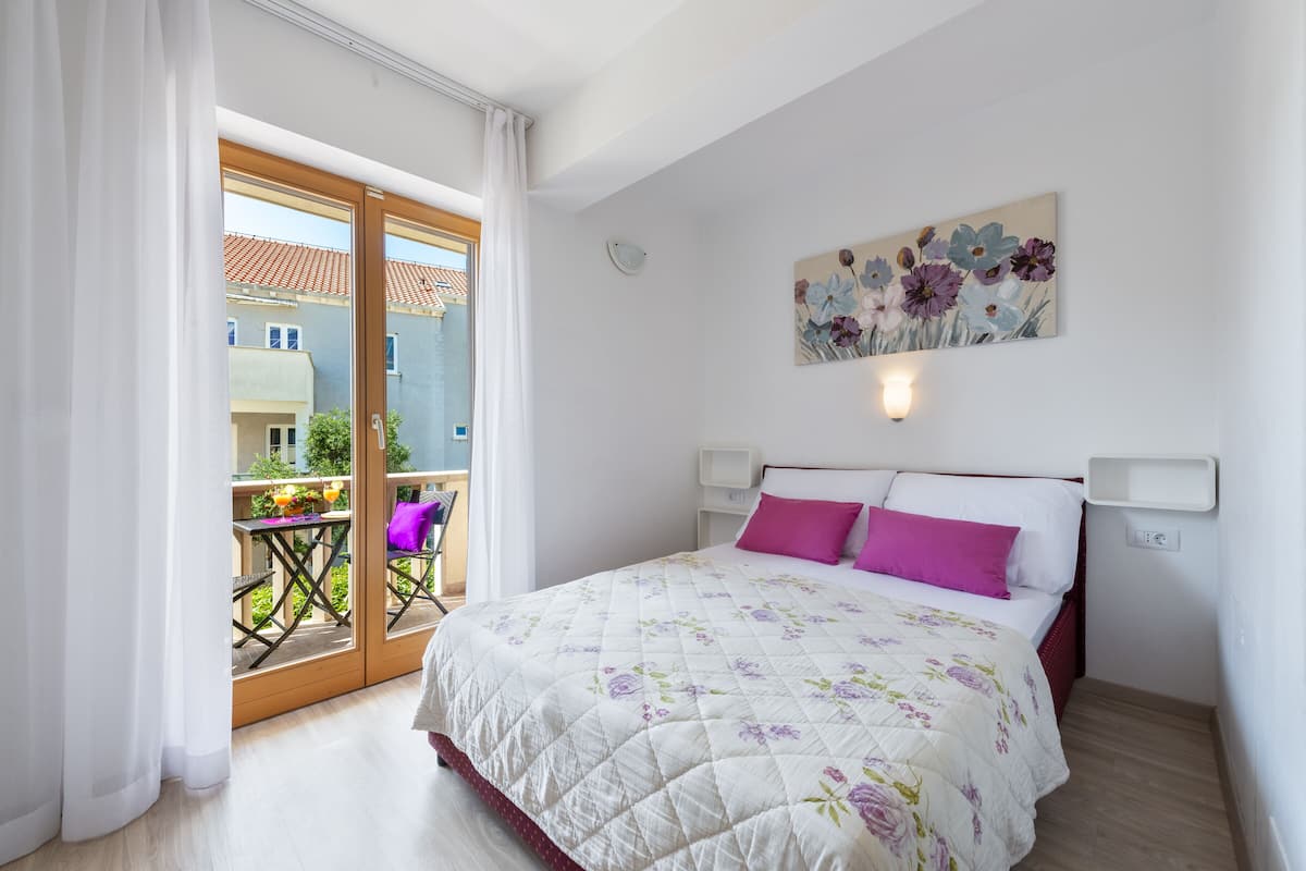 A bedroom with a bed, a balcony, and a painting on the wall.